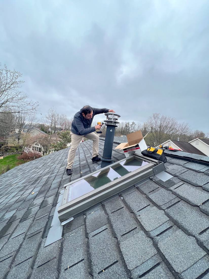 Installing a rain cap on a roof vent beside a skylight